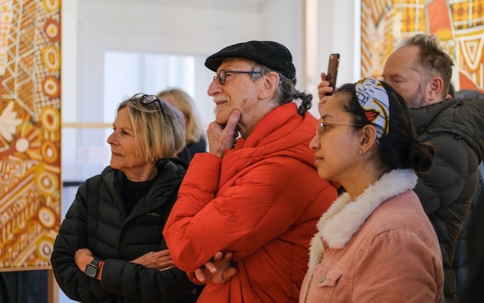 A group of people stand in a gallery space, gazing towards the same direction absorbedly.