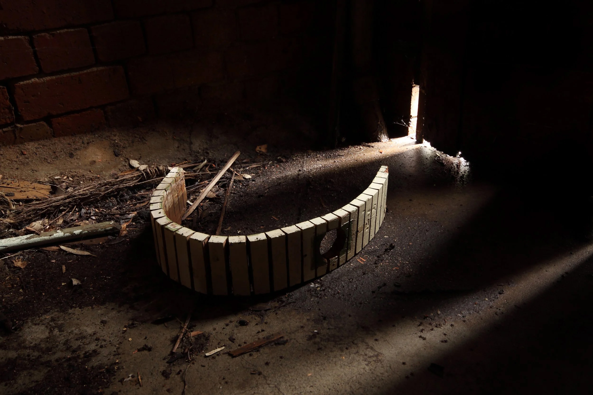 Curved wood bricks on a dusty floor with sunlight streaming through a narrow opening in a dimly lit space.