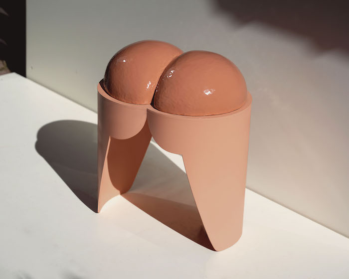 A pink fleshy stool that looks like a pair of butt cheeks sits on a white plinth.